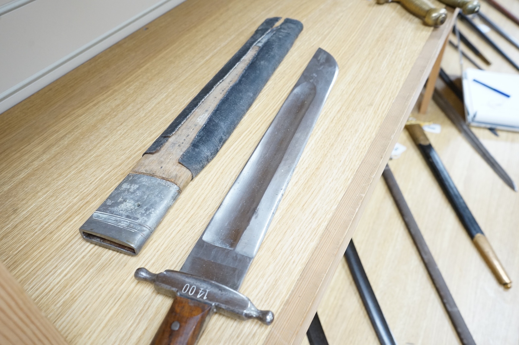 A 19th century Austrian military fascine knife, regulation iron crosspiece, two piece riveted wooden grips, in its wooden scabbard with iron mounts, leather covering loose